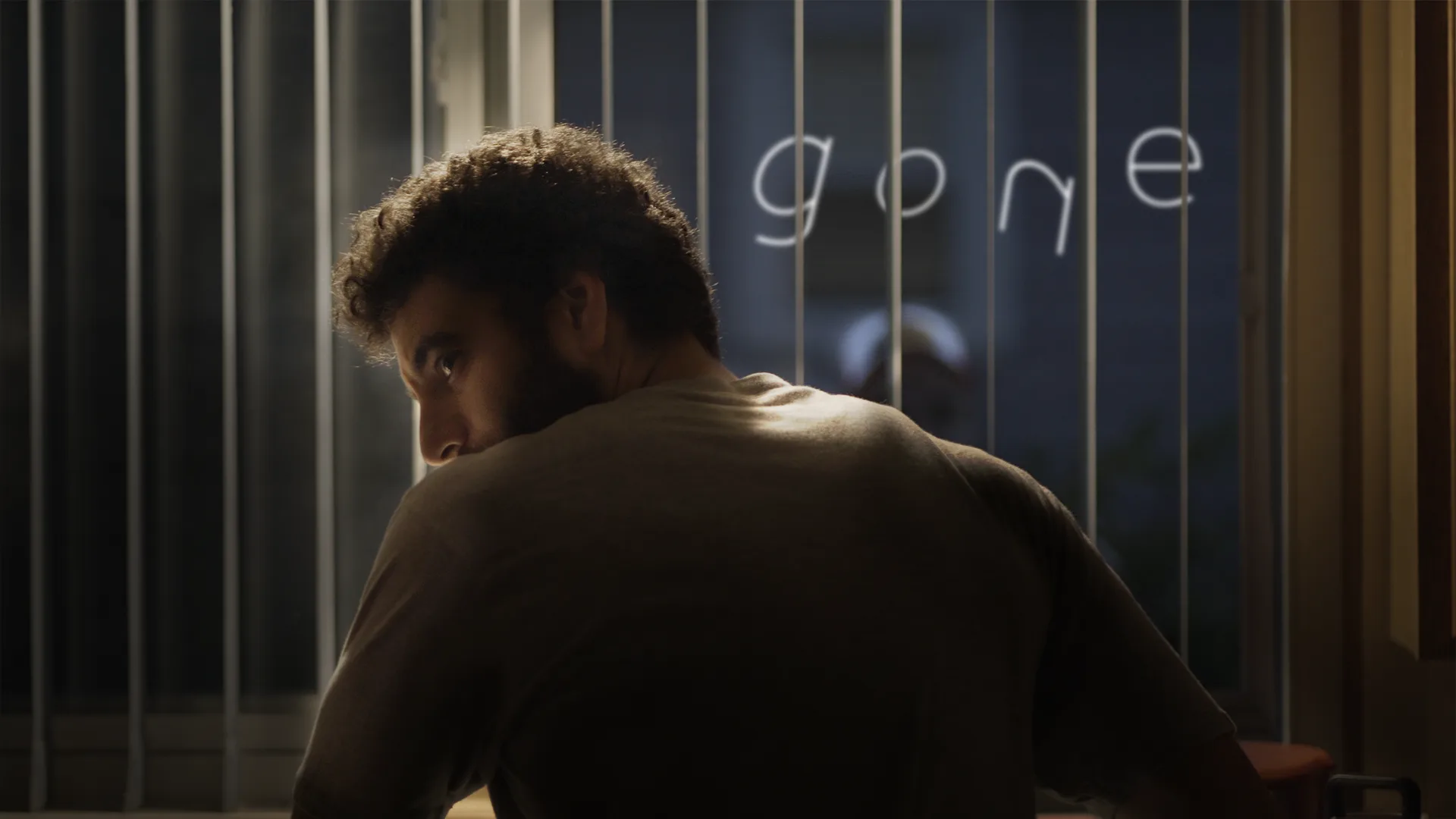 Gone poster: Joe looks back over his shoulder in a dark room, the word gone glowing in the window behind the blinds